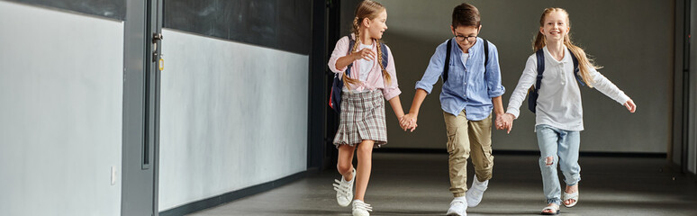 A group of young students, confidently strides down a brightly lit school hallway.