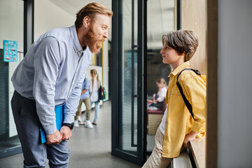 A man stands next to a little boy in a bright classroom, offering guidance and instruction.