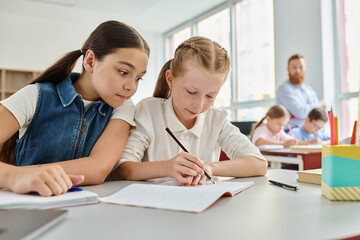 Two young girls are sitting at a table, immersed in their books, as they focus on reading and learning.