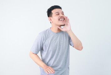 Young happy asian man announcing information with hands cup around mouth isolated on white studio background. advertising concepts
