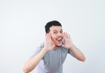 Young happy asian man announcing information with hands cup around mouth isolated on white studio...