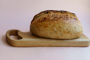 classic sourdough artisan bread with the addition of dried onions and onions on a wooden board on a pastel pink background.