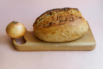 classic sourdough artisan bread with the addition of dried onions and onions on a wooden board on a pastel pink background.