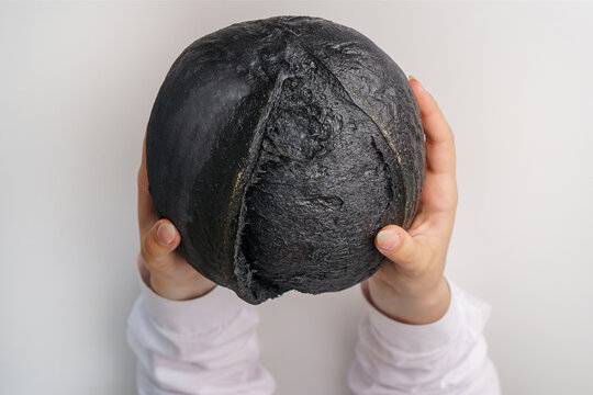 Creative and unusual handmade black sourdough artisan bread in the hands of a girl on a white background.