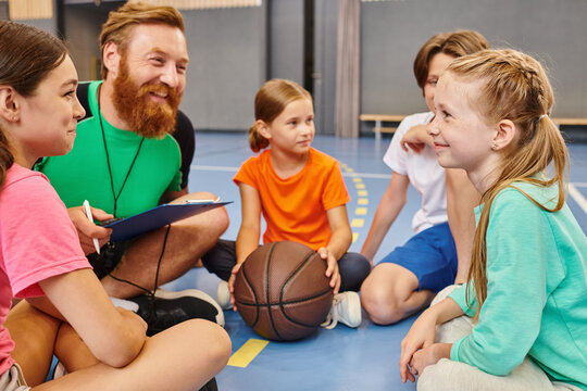 A diverse group of children sit attentively around a basketball as their male teacher instructs them in a bright, lively classroom setting. - Powered by Adobe