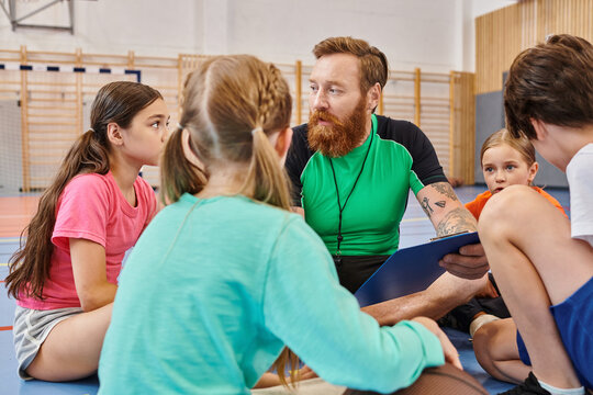 A diverse group of people, including children and their male teacher, are seated around each other in a gym, engaged in a lively and vibrant learning session.