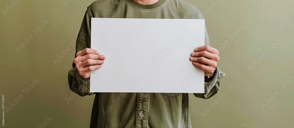 Poster Top view of a man holding a blank sheet of paper against an olive background for design purposes creating a mockup with copy space image