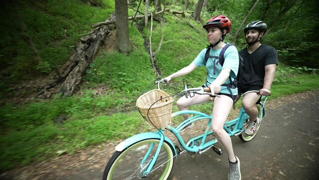 Front view of young fun couple cycling together on a tandem bike, cheerful smiling and having fun together on a paved trail along Potomac River C and O Canal.