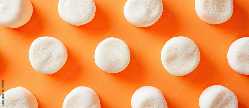 Poster Top down perspective displaying delectable marshmallows arranged in circles set against an orange background with ample copy space image