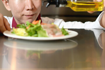 オリーブオイルをサラダにかける男性料理人