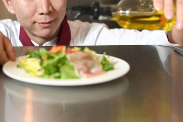 オリーブオイルをサラダにかける男性料理人