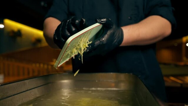 close up in a restaurant in a rib bar in the central hall chef in black gloves pours grated potatoes into an iron container