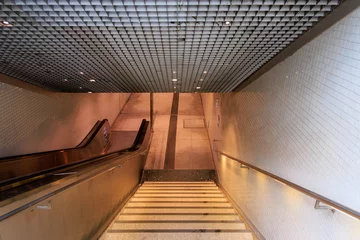 Fotobehang Gang A long, narrow, white subway tunnel with a staircase leading up to the top  © Jakapan
