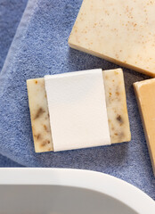 Soap bar with blank label on blue towels near vessel sink in bathroom, packaging mockup
