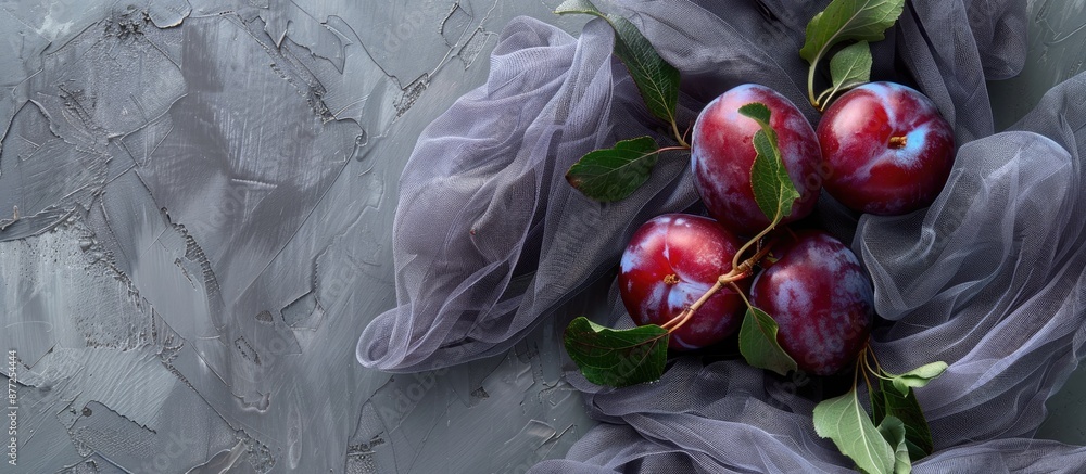 Aufkleber fresh ripe plums with leafs are displayed on a table with grey gauze fabric seen from above offering