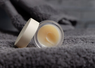 Opened lip balm jar with blank lid on dark grey bath towel closeup, cosmetic mockup