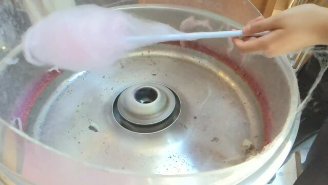 Cinematic shot of young woman hands spin cotton candy on machine. The concept of street food with a delightful treat for all ages, fun, and festive
