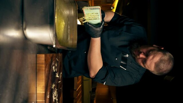 vertical video in a restaurant in a rib bar in the central hall chef in black gloves pours grated potatoes into an iron container