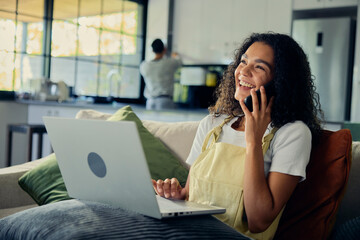 A woman sitting on a couch, using a laptop, and talking on a cell phone
