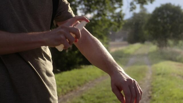 Prevention against mosquito bite during sunny summer day. Man is applying insect repellent on his hand.