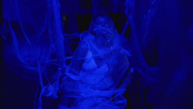 woman covered with cobweb standing in dark corridor illuminated by creepy blue light scary and mysterious atmosphere suitable for halloween