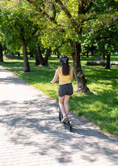 Girl rides a scooter along bicycle paths in the city in the summer.