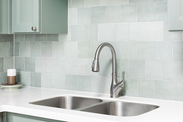 A faucet detail in a kitchen with sage green cabinets, square tile backsplash, and white marble countertop.