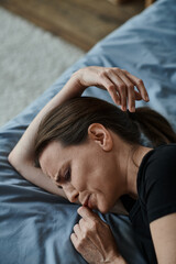 Fototapeta premium Middle-aged woman lying in bed, hand on head, lost in thought.