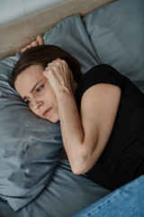Middle-aged woman laying down, holding head in hand with contemplative expression.