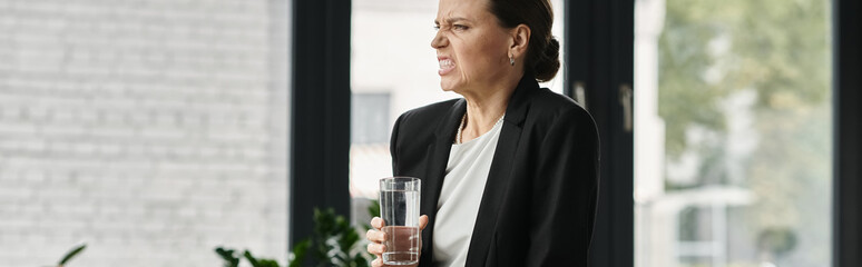 Woman holding glass of water in front of window.