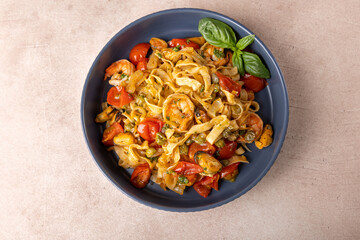 Noodles with shrimps, mussels, tomatoes, onions and capers. Pasta is served with olive oil and pesto sauce. Homemade traditional Mediterranean cuisine. Selective focus, close-up.