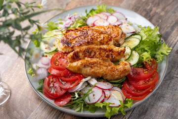 Warm salad with baked chicken breast and fresh vegetables, dressed with olive oil on a wooden background. Home kitchen in rustic style. Hearty delicious food. Selective focus, close-up.