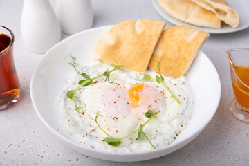 Turkish eggs (chilbir) with yogurt, fragrant butter, pea sprouts, flatbread and tea. Traditional Turkish breakfast with poached eggs (with liquid yolk). Selective focus, close-up.