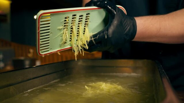 vertical video close up in a restaurant in a rib bar in the central hall chef in black gloves pours grated potatoes into an iron container