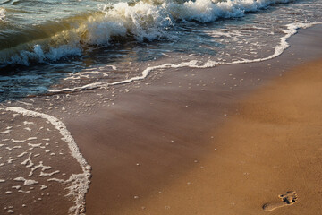 Photo of a sea wave on a sandy beach. Footprint of a man on the sand  