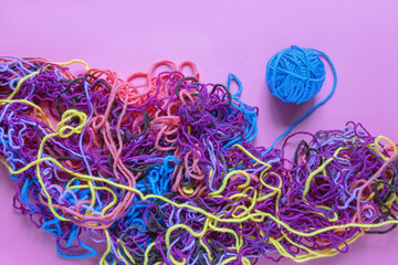 Colorful tangled threads and attempt to wind them into ball. Pink background, flat lay, copy space