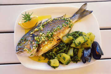 Balkan cuisine. Grilled fish ( sea bream ) with green leafy vegetables on white rustic table
