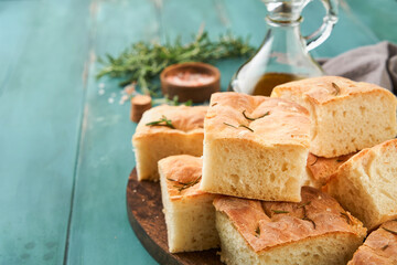 Focaccia. Italian traditional bread and pastry recipe cut into pieces for serving with olive oil, aromatic seasonings and rosemary on old wooden rustic table background.Top view. Place for text.
