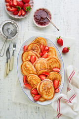 Pancakes stacked on white ceramic plate with sugar powder, jam and strawberry on old rustic light wooden background. Idea for serving breakfast, lunch or snack. Summer berry breakfast. Top view.