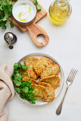 Vegetable zucchini fritters in with sour cream pepper and olive oil served on rustic plate on old cracked tile table background. Healthy vegetarian food. Cover or article. Top view. Place for text.