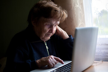 An elderly woman typing on a laptop keyboard, learning on her own at home.