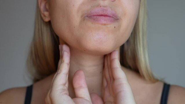 Young blonde woman with throat ache touching enlarged inflamed lymph nodes under jaw on her neck on dark grey background. Flu, cold, covid, tonsillitis, sars virus, inflamed tonsils. Sore throat
