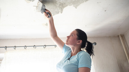 a woman using a spatula removes the top layer of old paint on the ceiling
