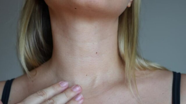 Young blonde woman touching her neck with her hands on a grey background. Lines on the female neck. Wrinkles, age-related changes, rings of Venus, creases, goosebumps