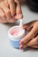 Hands scooping pink cream from a blue jar