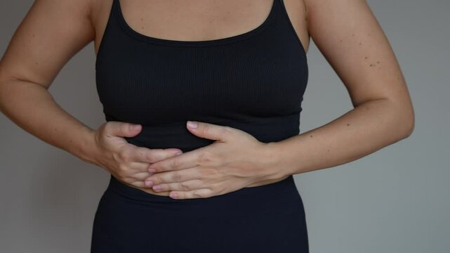 Young woman holding her side under the right rib with her hands on a grey background. Severe stomach pain, diseases of the gallbladder and liver, attack of cholecystitis, dyskinesia, gallstones