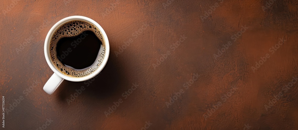 Poster desk with a white mug of hot coffee seen from above on a brown surface offering a place for your tex