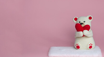 Knitted toy polar bear holding a red heart on a pink background, copy space for text