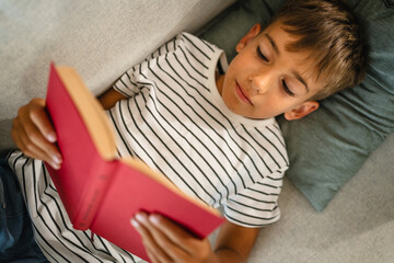 young small caucasian boy lying on the sofa and read a book