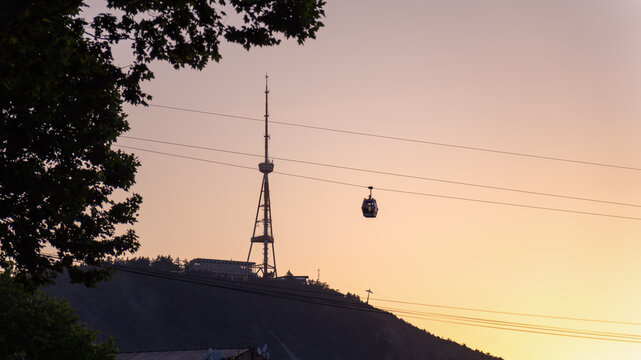 Cableway cabin on the background of a mountain with a lightning rod at sunset. Cable car in Tbilisi on the background of Mtatsminda mountain at sunset.
